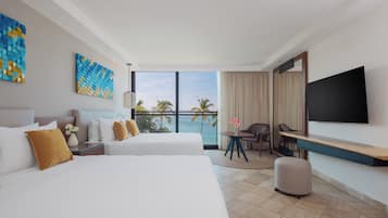 A hotel room with two beds, a desk, a TV, and a view of the ocean.