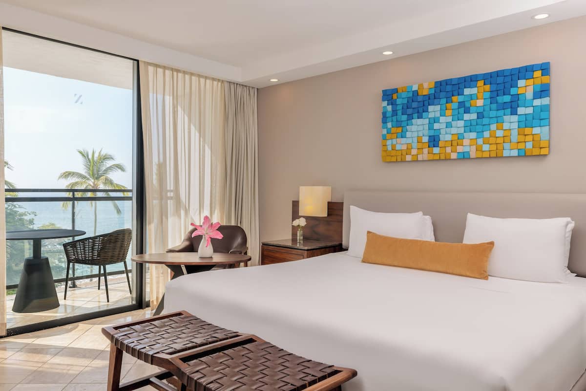 Habitación de hotel con una cama grande, vistas a palmeras, un balcón y un cuadro abstracto moderno en la pared.