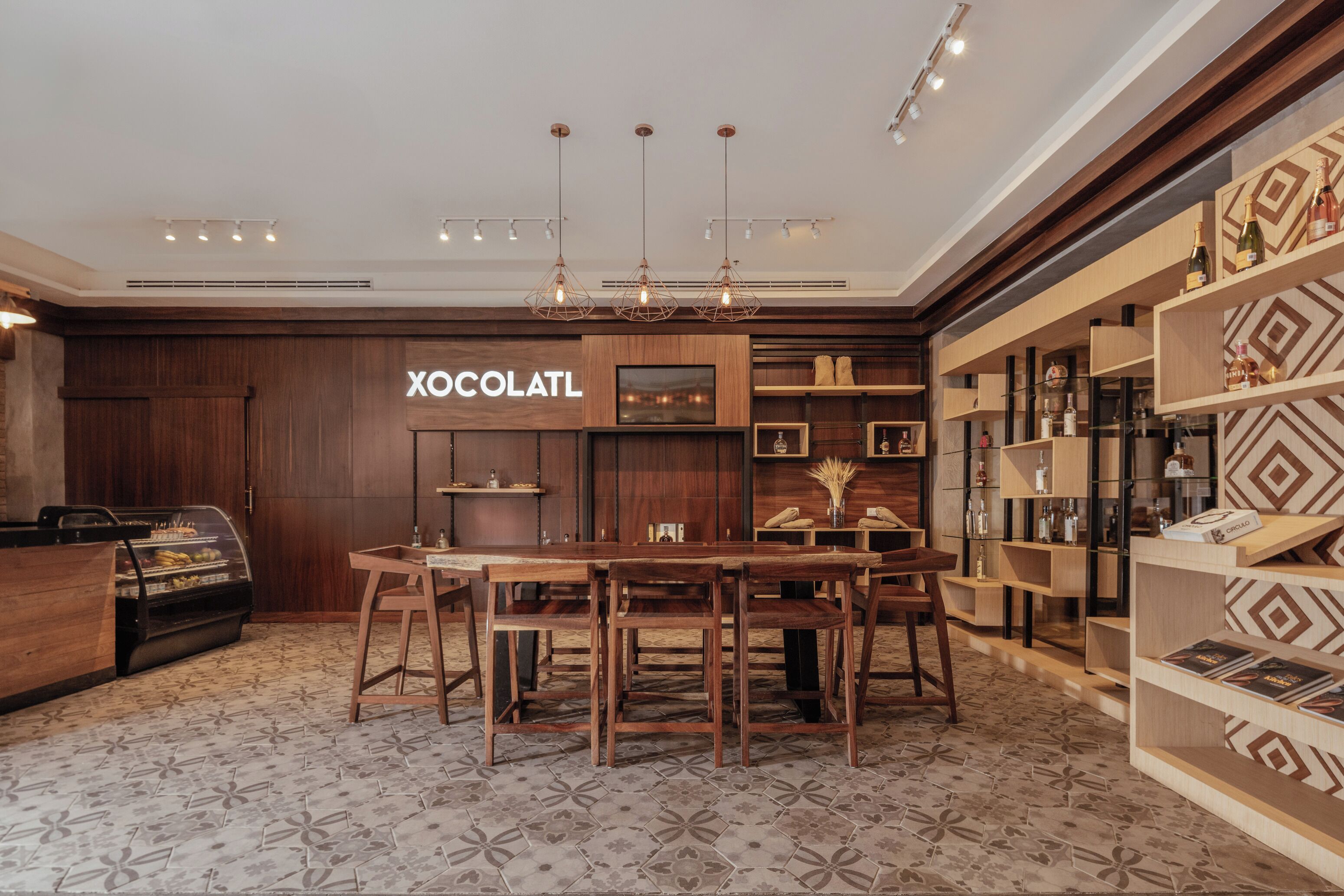 Un intérieur moderne avec un comptoir d’accueil en bois, un coin repas avec une grande table et des chaises, et un téléviseur fixé au mur.