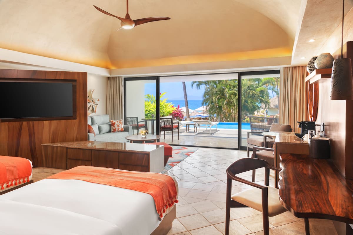 Habitación de hotel con una cama grande, escritorio, silla, televisor y vistas a una piscina y palmeras.