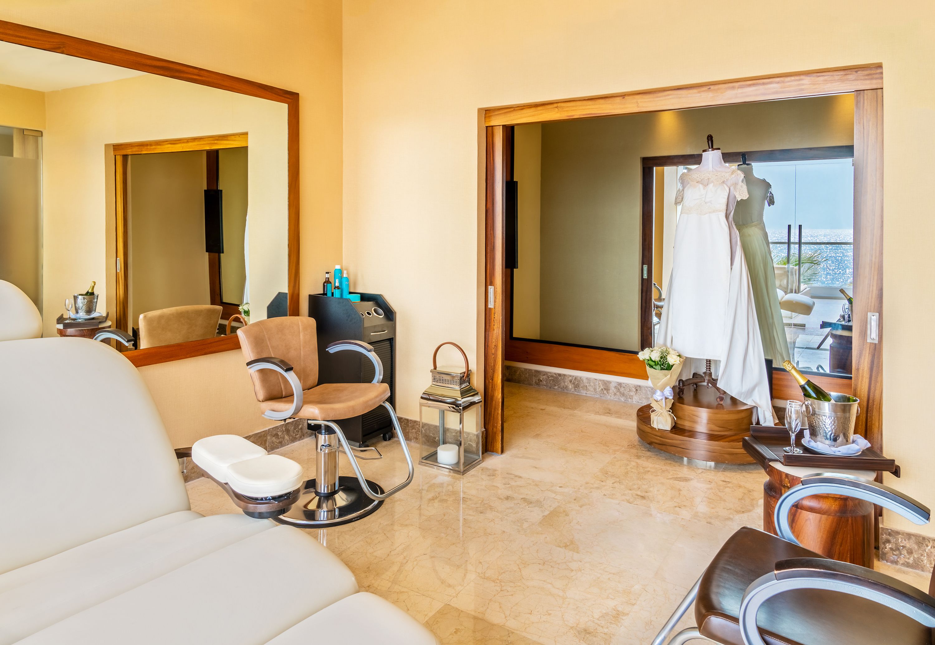 Quarto de hotel com uma cama grande, área de estar com uma poltrona e uma pequena mesa, toucador com espelho e vista para o mar através de uma porta de vidro.