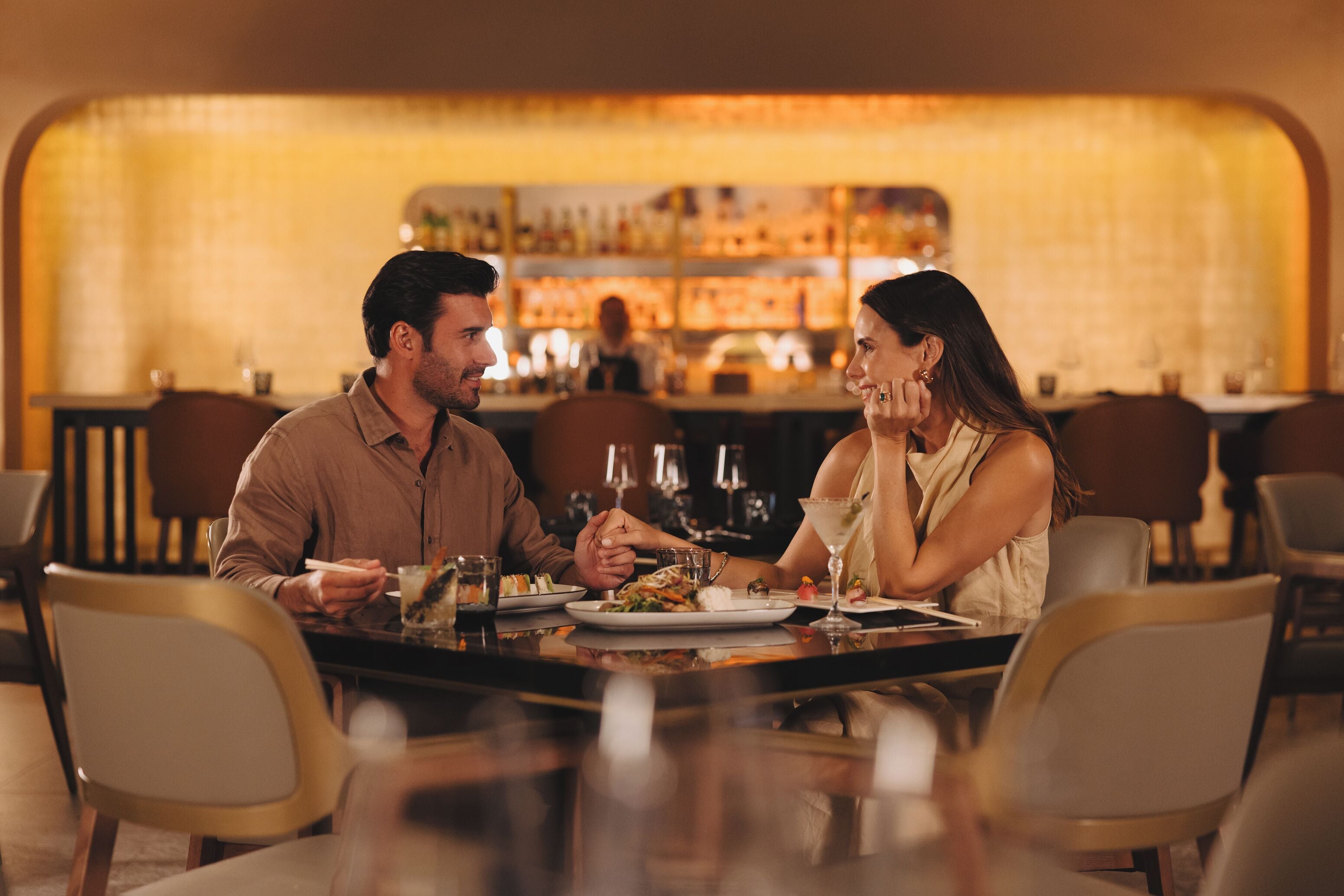 Una pareja cenando en un restaurante, con una barra de fondo.