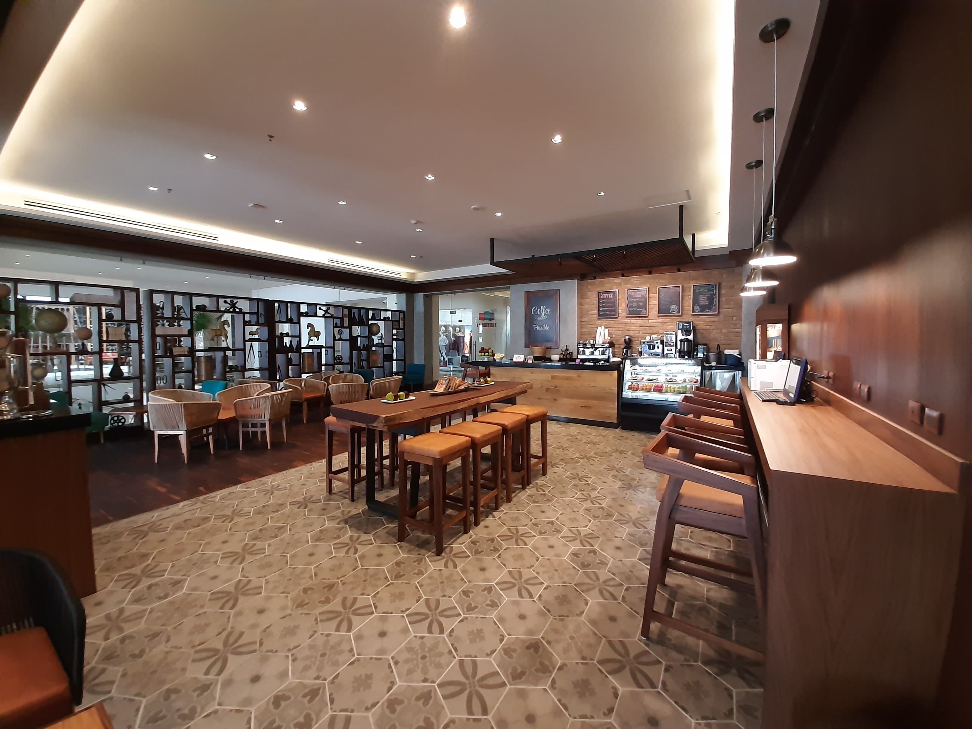 A modern cafe with wooden furniture, hexagonal patterned flooring, and a coffee bar with a menu board.