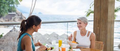 Two people dining at a wooden table with a view of the ocean and palm trees.