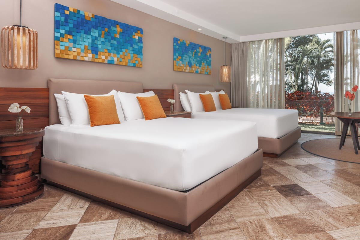 Habitación de hotel con dos camas, cabecero de madera, una mesita redonda y vistas al exterior.