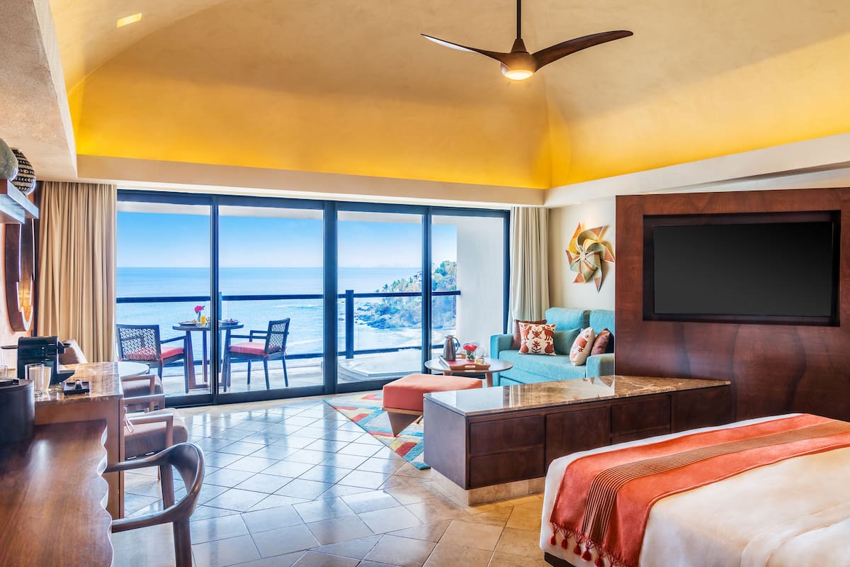 Habitación de hotel con balcón, televisión, escritorio y cama.