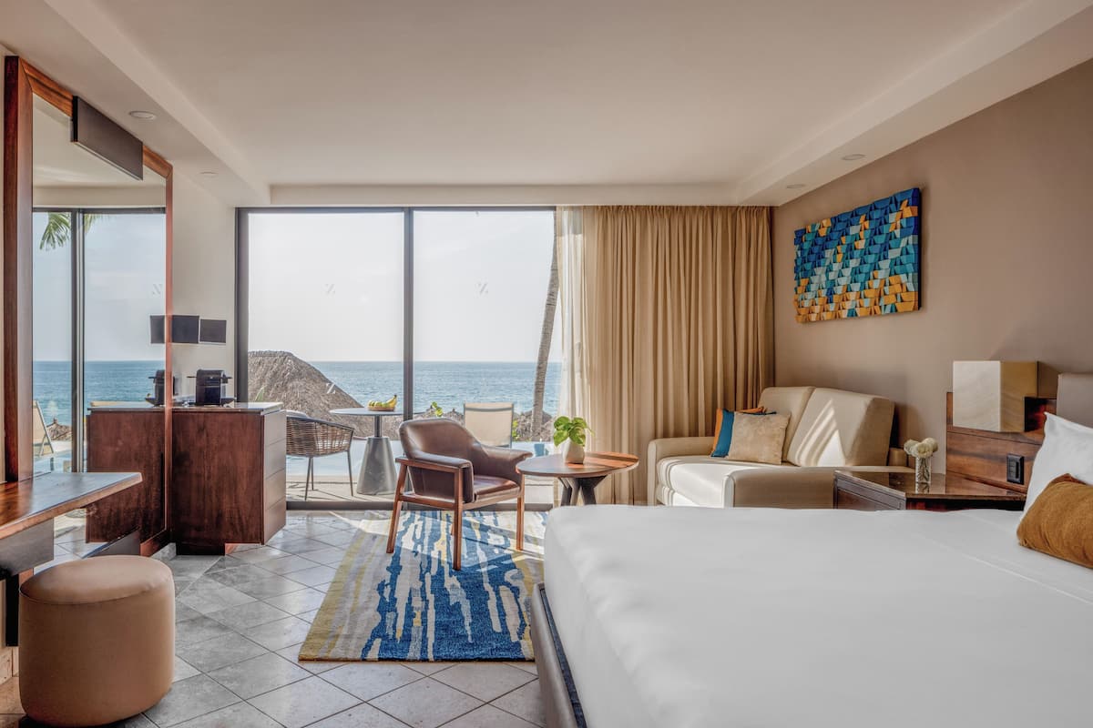 Habitación de hotel con una cama grande, un escritorio, una silla y vistas al océano.