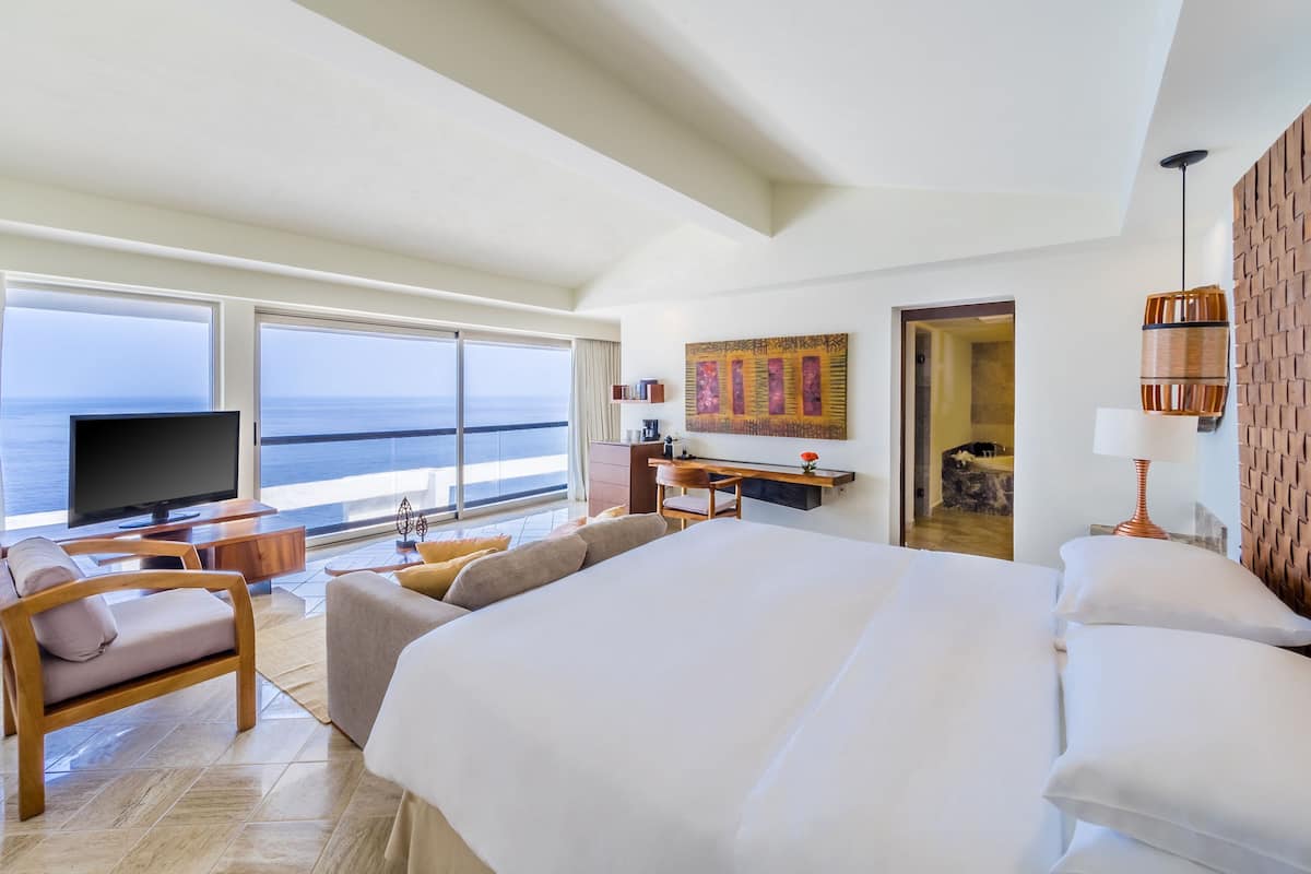 Amplia habitación de hotel con una cama grande, televisión, escritorio y vista al océano.