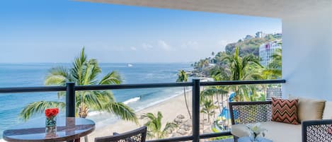 A balcony with a view of the beach and ocean, furnished with wicker chairs and a small table.