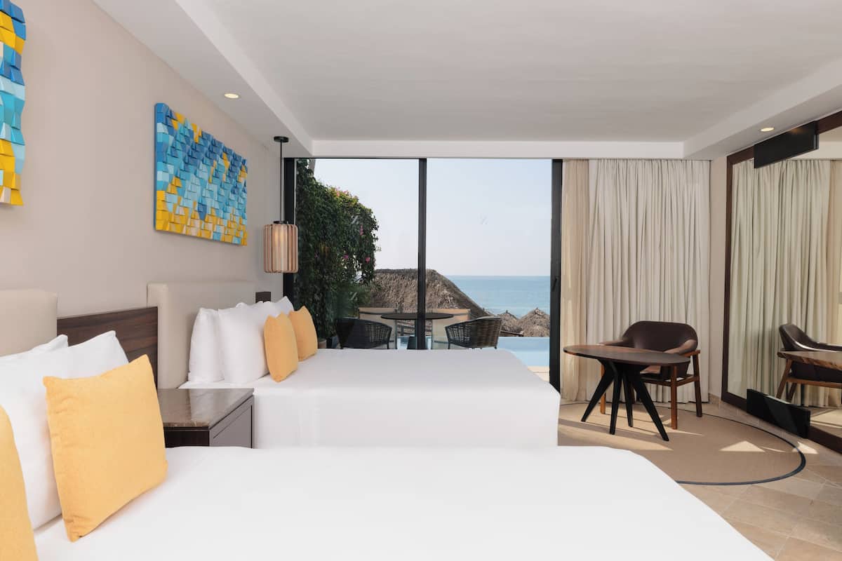 Habitación de hotel con dos camas, un comedor y vista al océano.