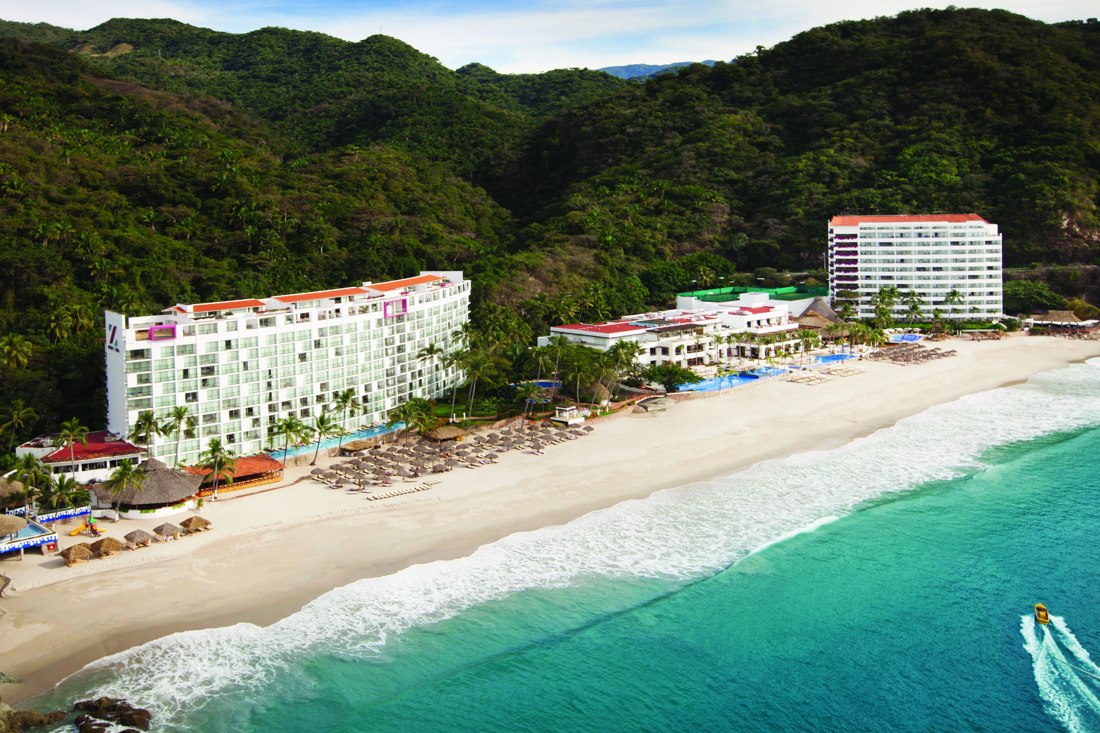 Un hotel frente a la playa con varias construcciones, una playa arenosa y una vista despejada del océano.