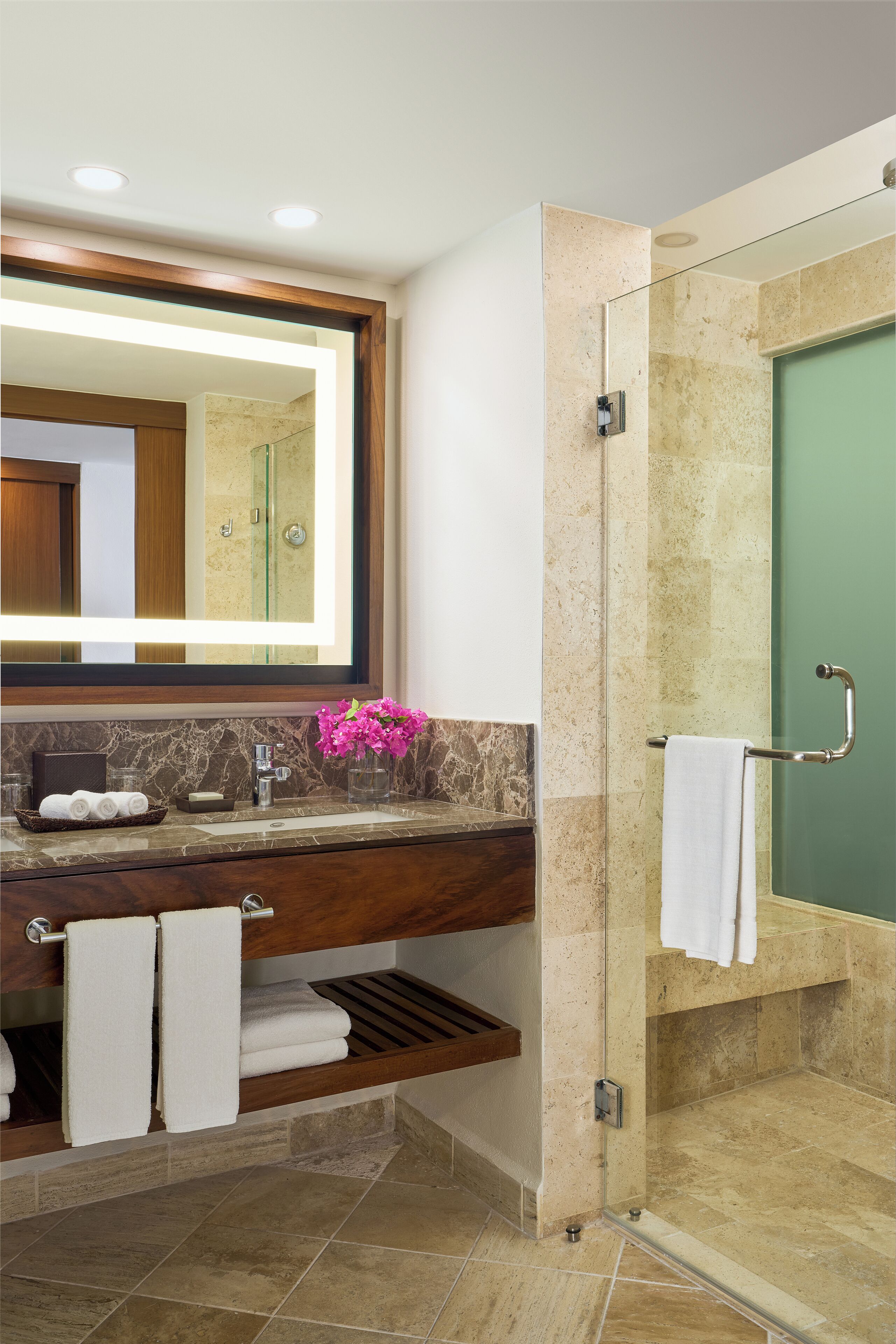 A modern bathroom with a marble sink, a large mirror, a glass shower enclosure, and a towel rack.
