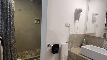 A bathroom with a shower, a sink, and a hairdryer mounted on the wall.