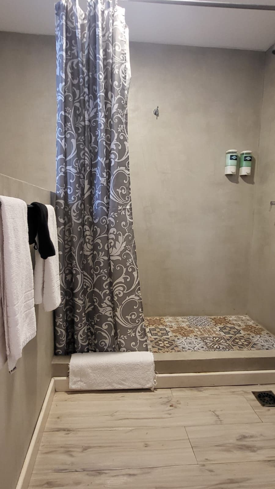 Área de duche com cortina estampada, um porta-toalhas com toalhas e uma pequena prateleira com produtos de higiene pessoal.