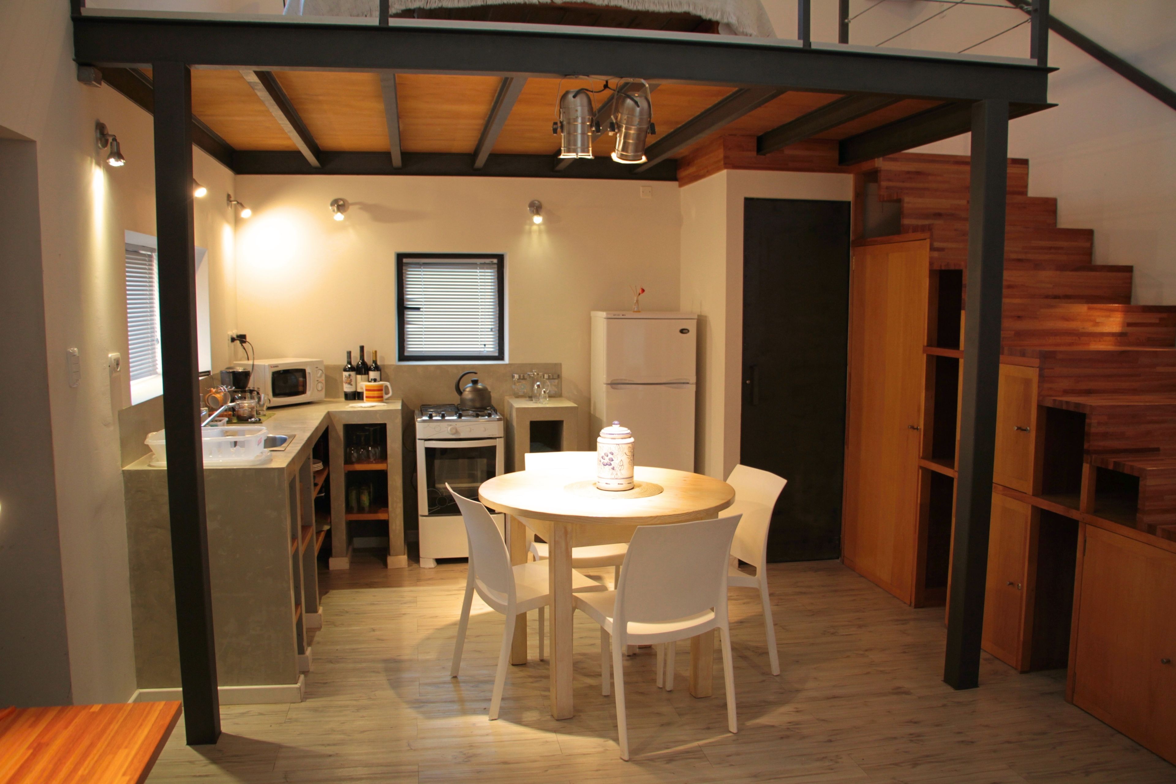 A compact kitchen with a dining area, wooden flooring, and a staircase.
