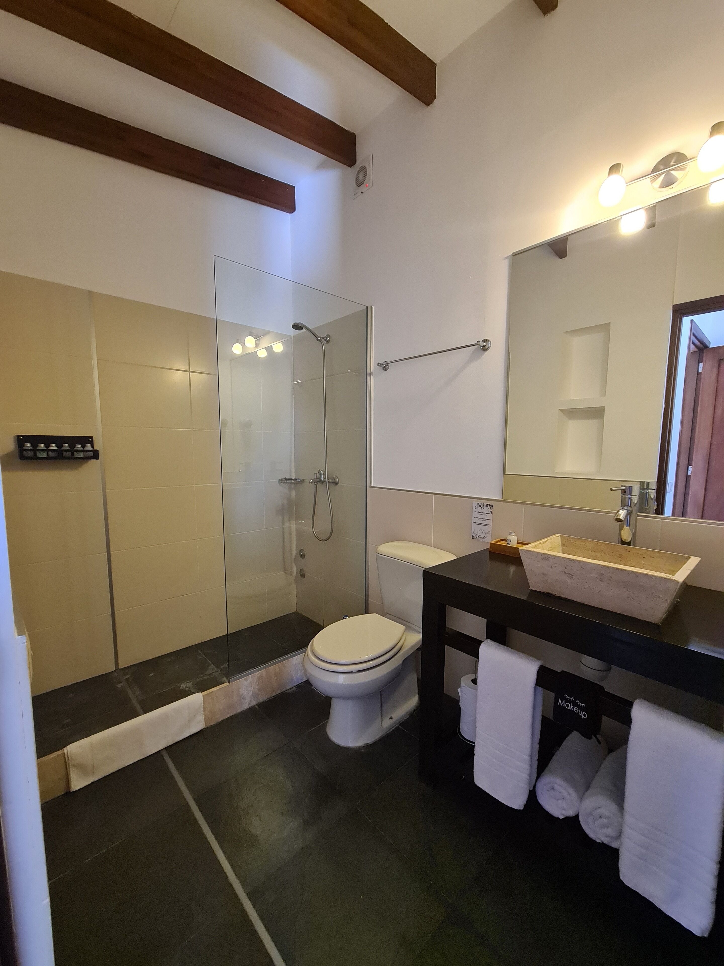 Un baño con ducha de vidrio, inodoro, lavamanos con espejo y un perchero para toallas.