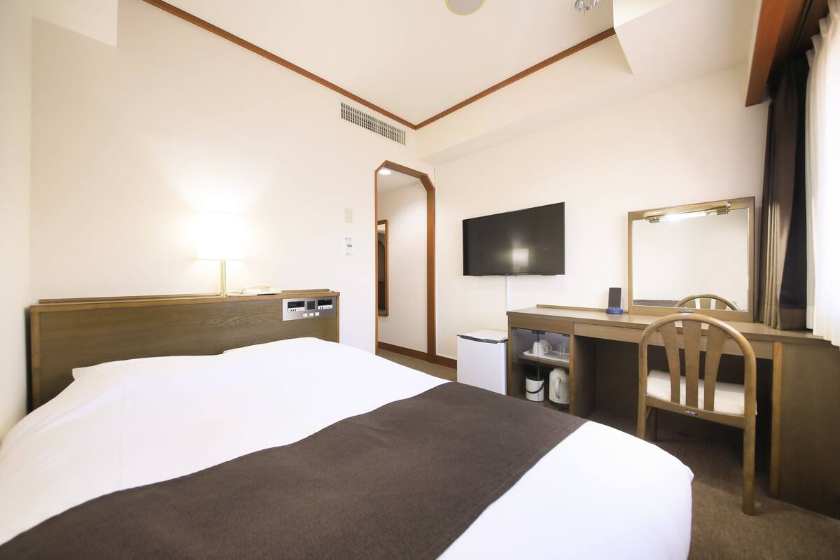 A hotel room with a bed, desk, chair, TV, and a mirror.