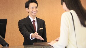 A hotel reception area with a reception desk, a man in a suit, and a woman. - Maple Inn Makuhari (Chiba)
