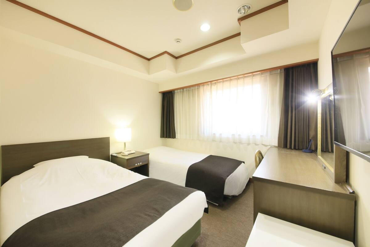 A hotel room with two beds, a desk, a mirror, and a window with curtains.