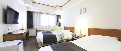 A hotel room with a bed, a desk with a computer, a TV, and a window with curtains.