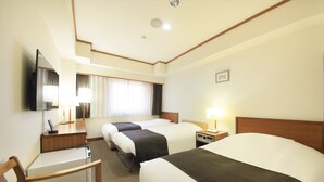 A hotel room with three beds, a desk, a chair, a TV, and a window with curtains. - Maple Inn Makuhari (Chiba)