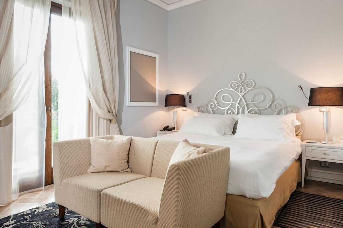 A hotel room with a bed, a sofa, a nightstand, a lamp, and a window with curtains.