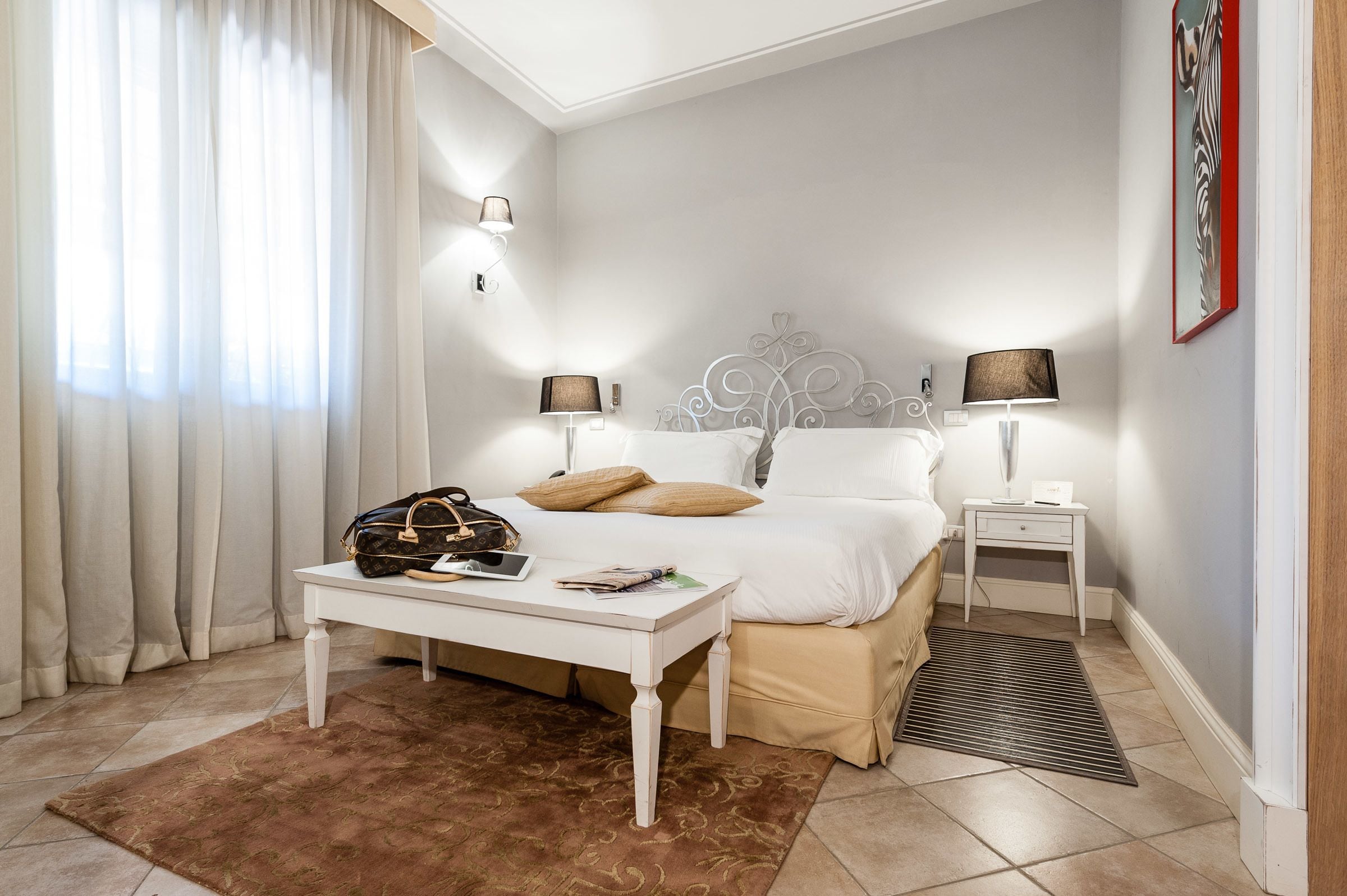 Une chambre bien rangée, avec un lit, des tables de chevet, une commode, un bureau et une fenêtre avec des rideaux.