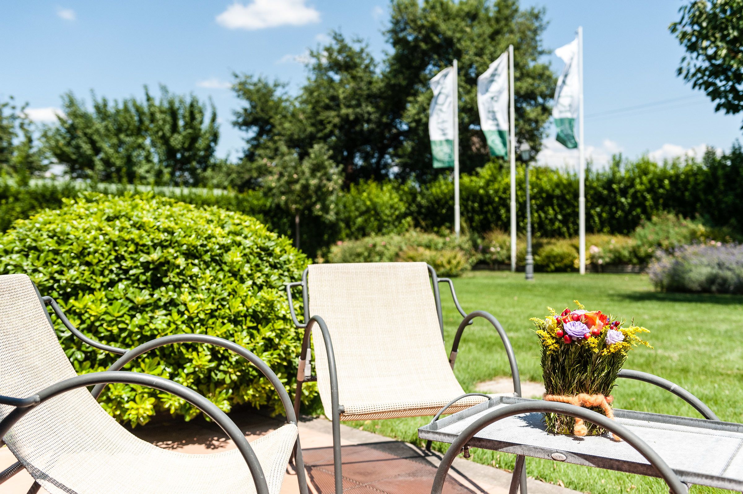 A patio area with two chairs and a table, surrounded by greenery and flags.
