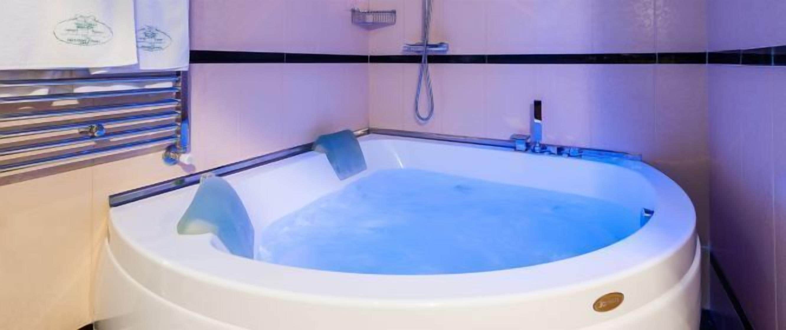 Una vasca idromassaggio bianca in un bagno, con un soffione della doccia sopra e un porta asciugamani a sinistra.