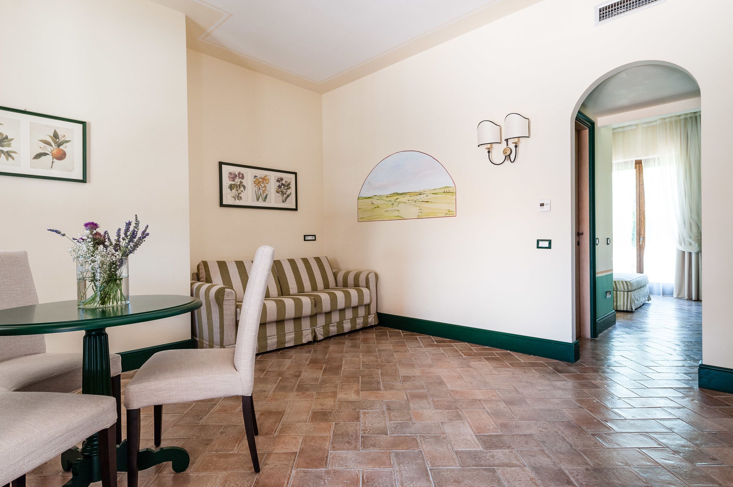 A room with a striped sofa, a round table with a vase of flowers, and a wall-mounted lamp.