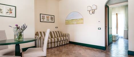 A room with a striped sofa, a round table with a vase of flowers, and a wall-mounted lamp.