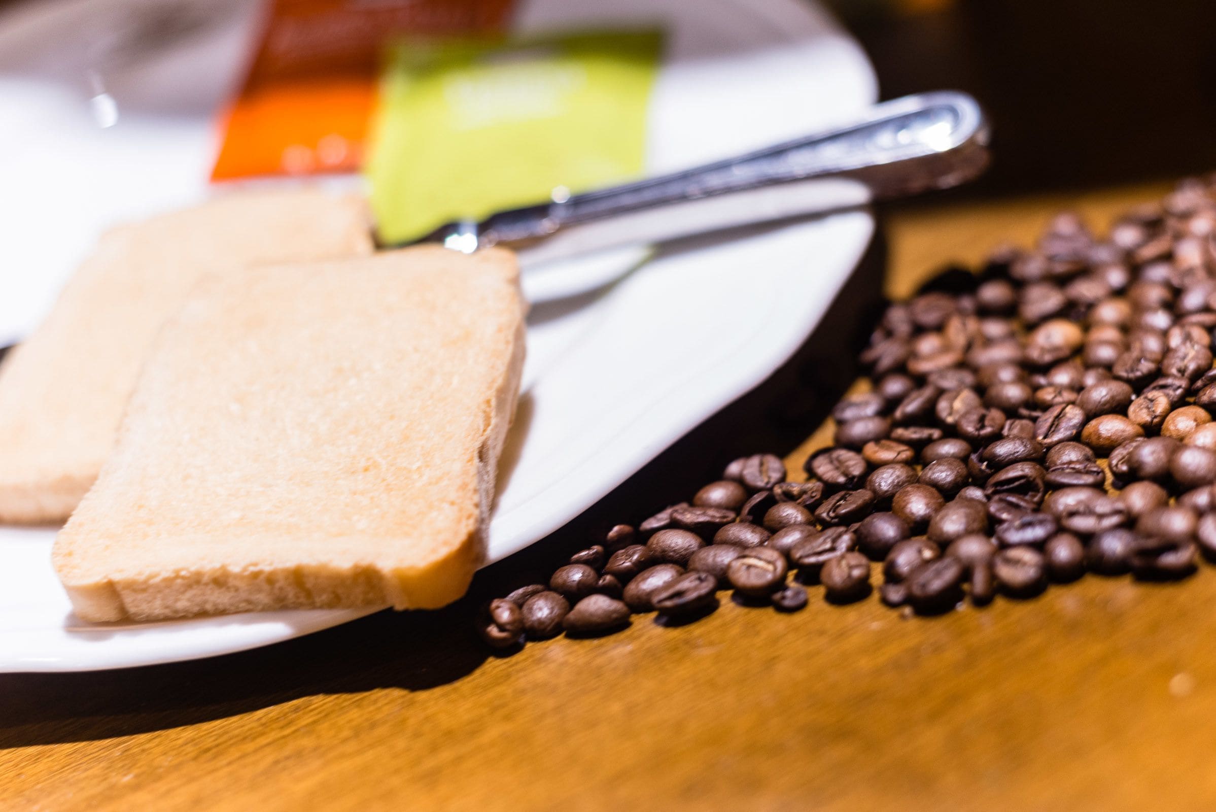 A plate with two slices of toast and a spoon, surrounded by coffee beans on a wooden table.