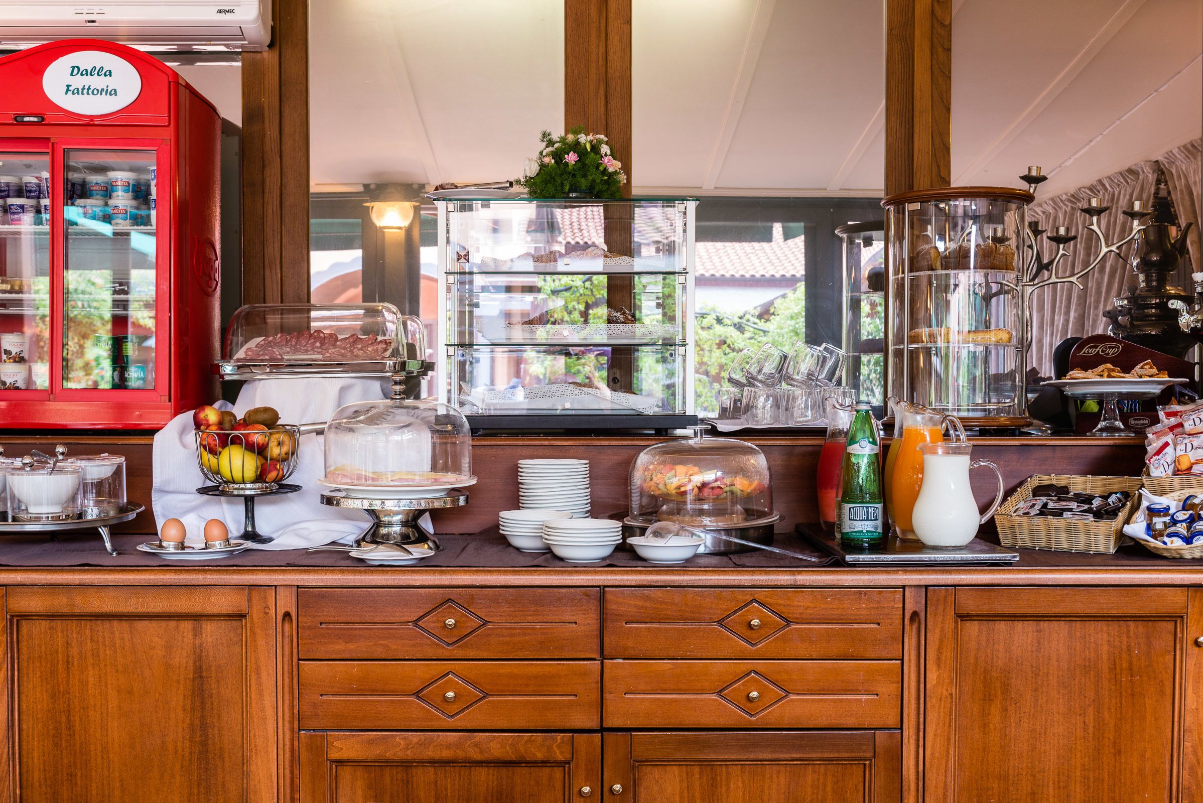 A breakfast buffet with various food items, a red milk cooler, and a coffee machine.