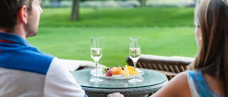 A couple seated at a round glass table outdoors with a view of a grassy area.
