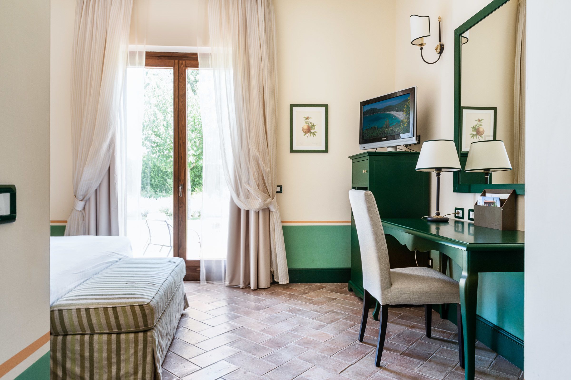 Ein Hotelzimmer mit Bett, Schreibtisch, Stuhl, Schreibtischlampe, Fernseher und einem Fenster mit Vorhängen.