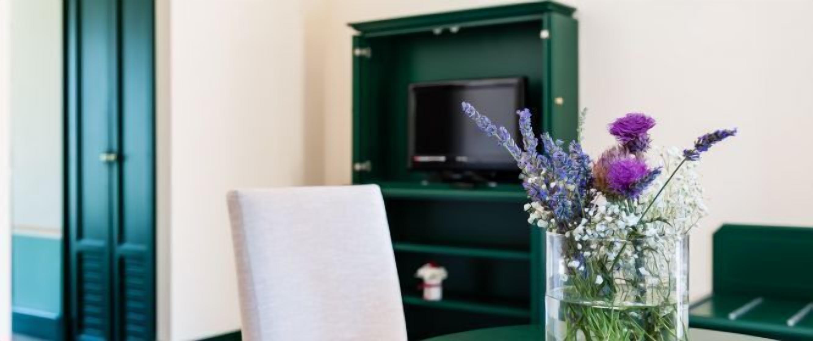 A room with a green bookshelf, a white chair, and a vase with flowers.