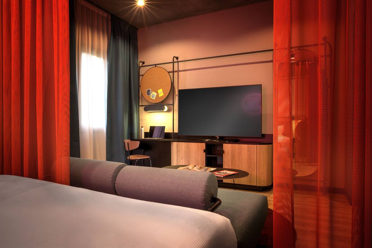 A hotel room with a bed, a TV, a small table, and a seating area.
