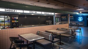 A restaurant with a counter displaying 'SHOULD I STAY OR SHOULD I GO' sign, seating area with tables and chairs, and a neon sign in the background. - Stay Hotel (Brunello)