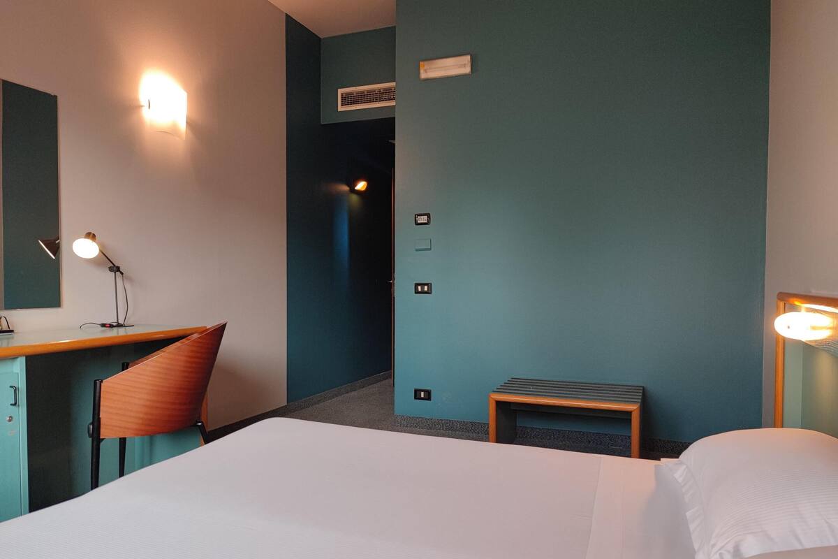 A hotel room with a bed, a desk, a chair, and a small table.