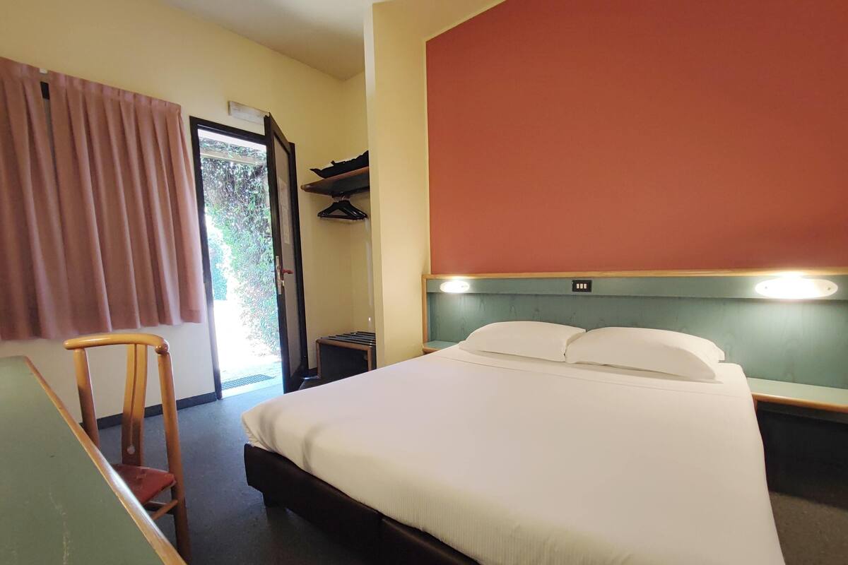 A hotel room with a bed, a chair, a desk, and a wardrobe.