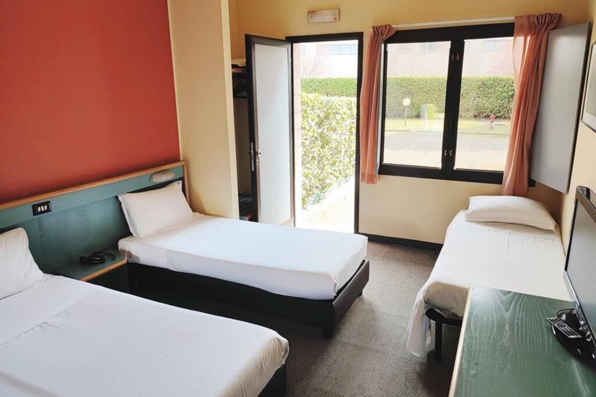A hotel room with two single beds, a desk with a computer, and a window with curtains.
