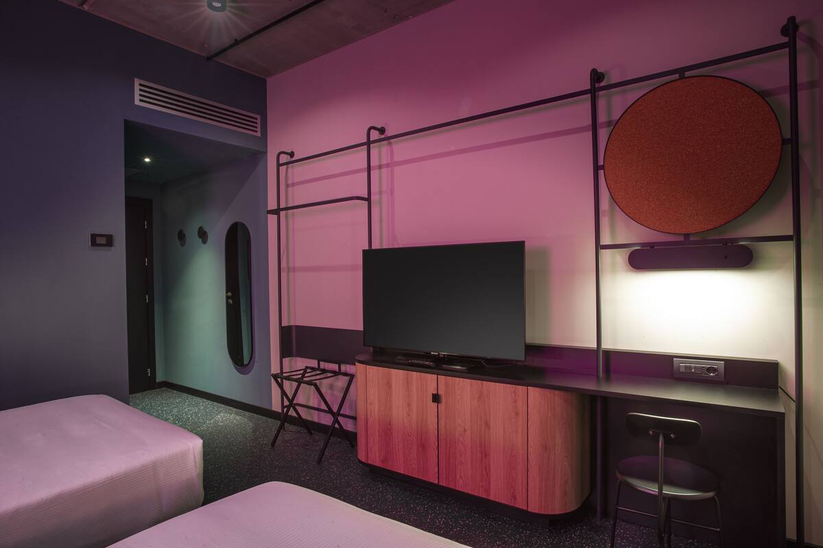 A modern hotel room with a bed, a TV, a desk, and a chair.