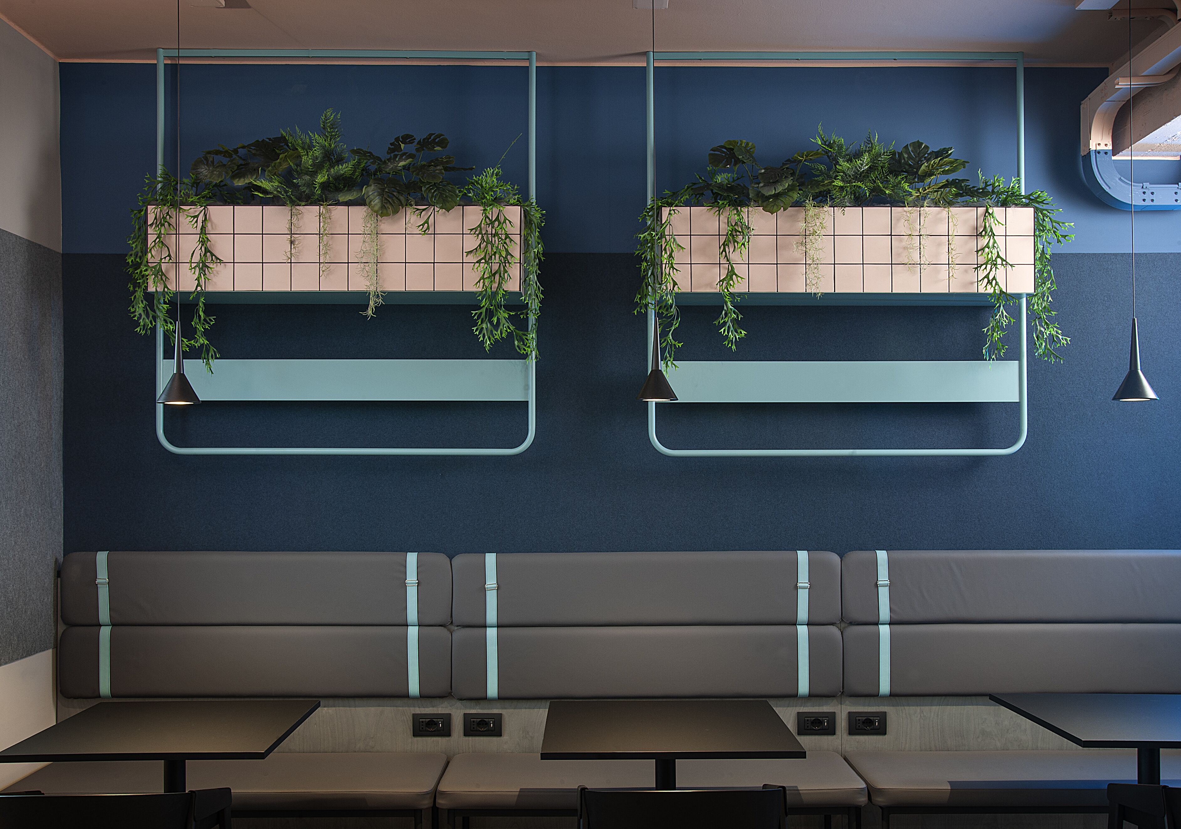 A modern restaurant interior with two seating areas, each featuring a bench and a table.