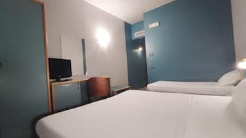 Una habitación de hotel con una cama grande, un escritorio con televisor, una silla y una mesita.