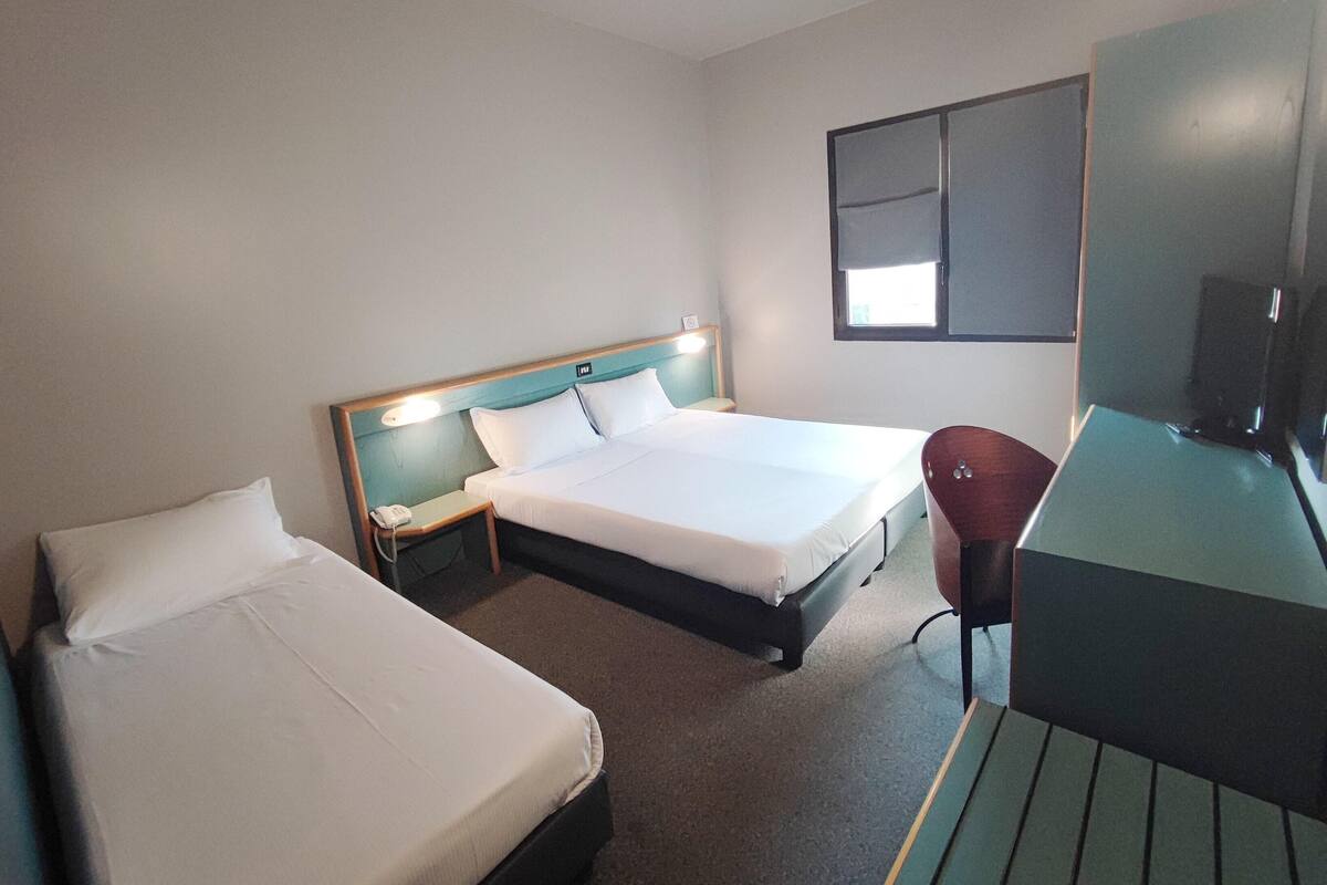 A hotel room with two single beds, a desk, a chair, and a TV.