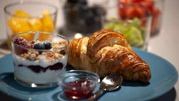 Een ontbijtplaat met een croissant, yoghurt met bessen en een klein potje jam.