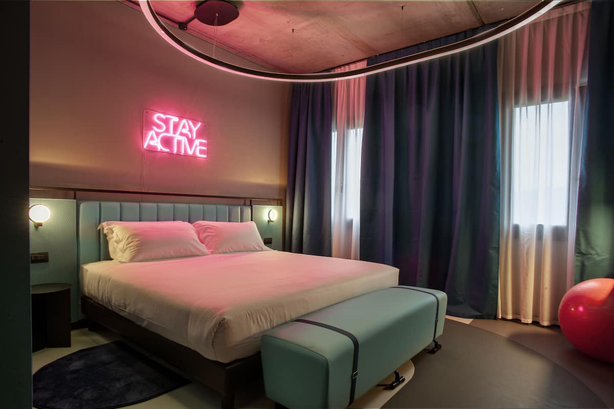A modern bedroom with a bed, bench, neon sign, and curtains.