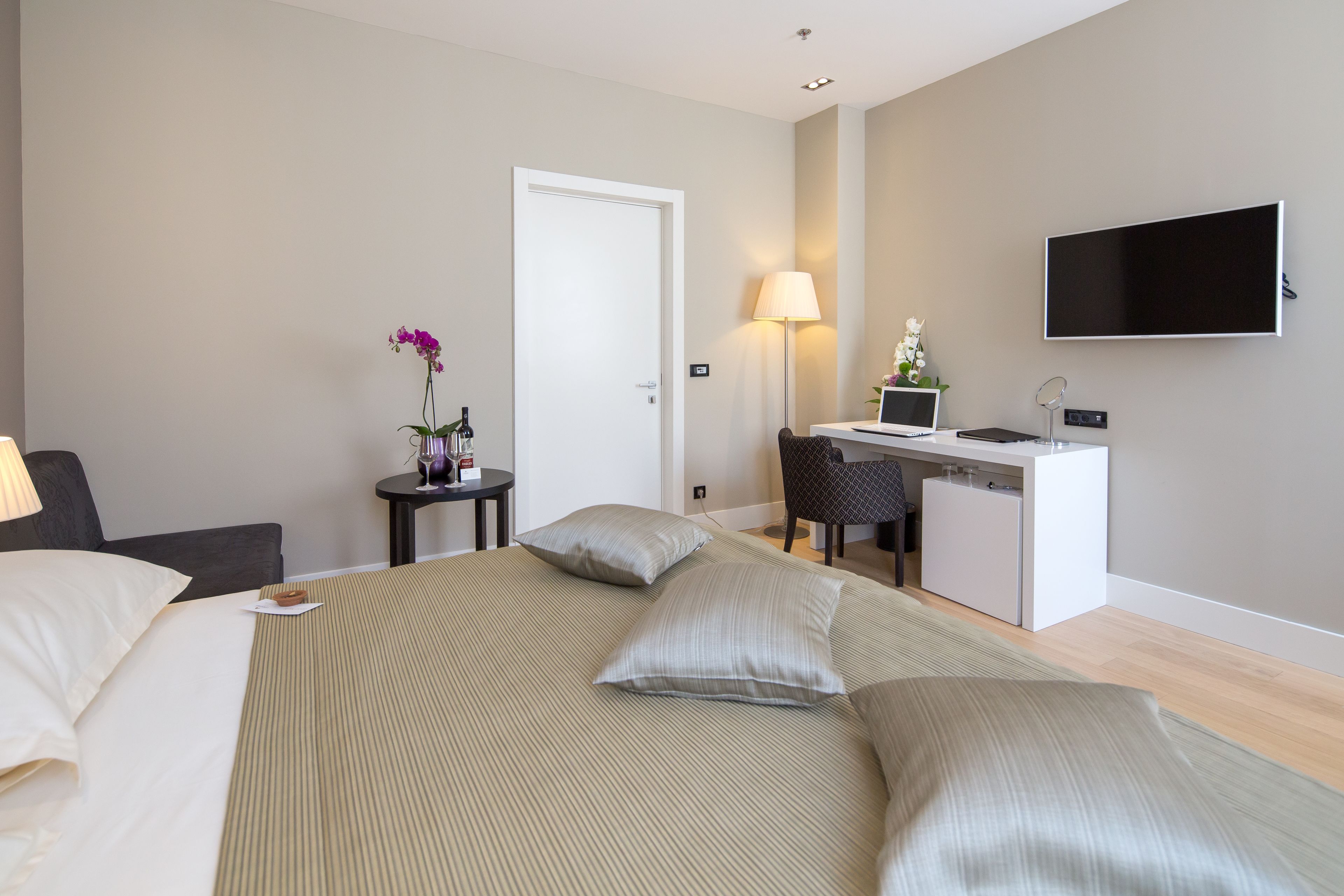 A hotel room with a bed, a desk, a chair, a TV, and a lamp.
