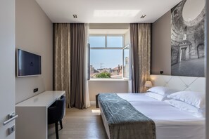 A hotel room with a bed, a desk, a chair, a TV, and a window with curtains.