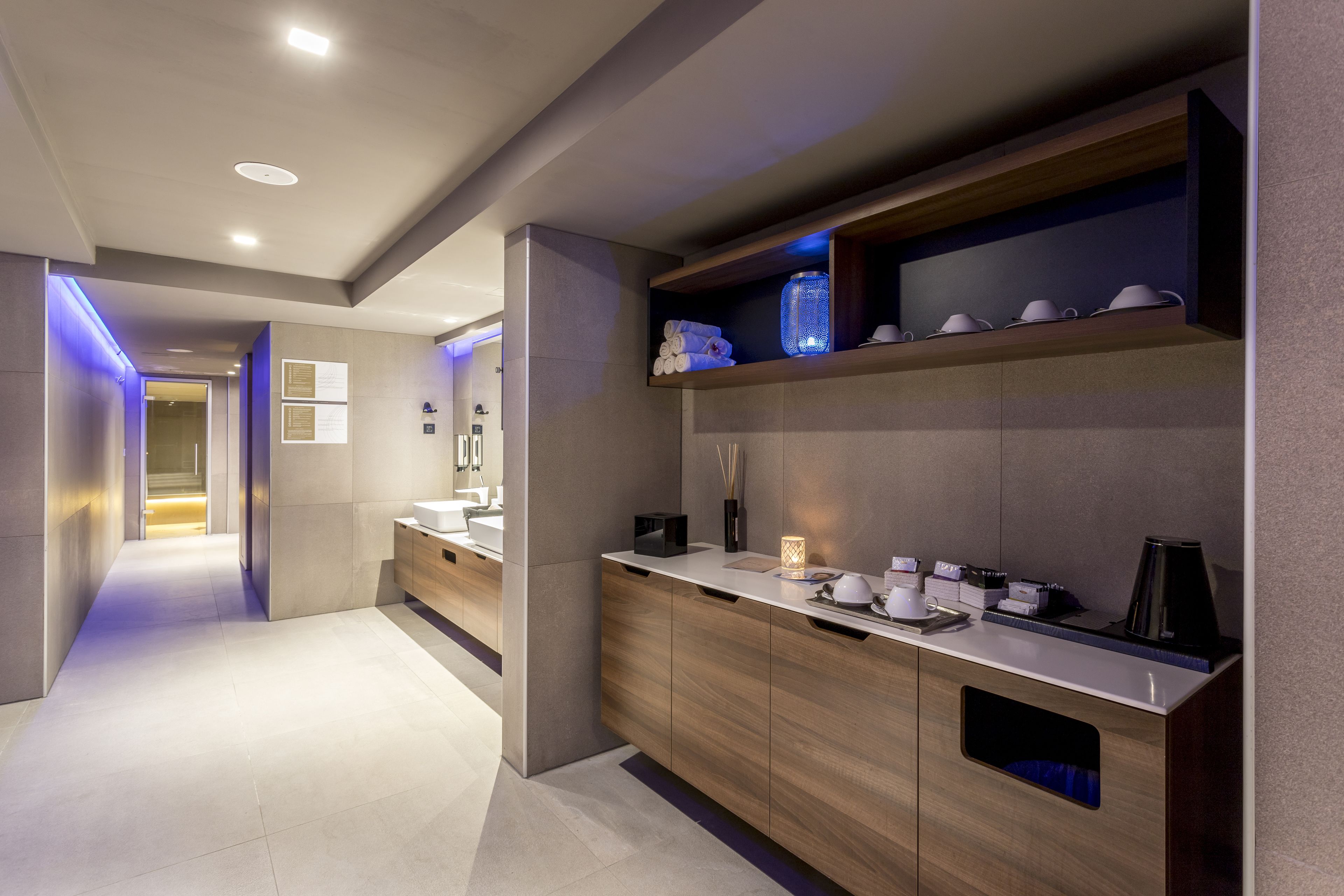 A modern hotel bathroom with a large mirror, wooden vanity, and a shelf with toiletries.